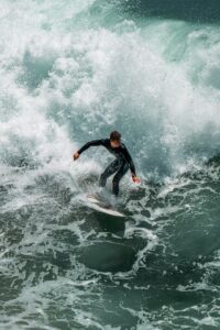 A surfer in a black wetsuit riding a large crashing wave
